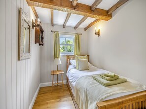 Un dormitorio con una cama de madera, una mesita de noche, un espejo, una ventana con cortinas y una viga de techo de madera.