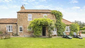 A brick house with a tiled roof, a front door, and a small garden with a lawn and two chairs. - 2 bedroom accommodation in Burgh Le Marsh (Burgh Le Marsh)