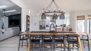 Eine moderne Küche mit Kochinsel, ein Essbereich mit Holztisch und -stühlen sowie ein Wohnbereich mit Sofa und Fernseher.