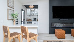 Ein modernes Wohnzimmer mit Fernseher, zwei Holzstühlen, einem Couchtisch und einer Küche im Hintergrund.