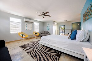 A bedroom with a bed, two chairs, a ceiling fan, and a zebra-patterned rug.