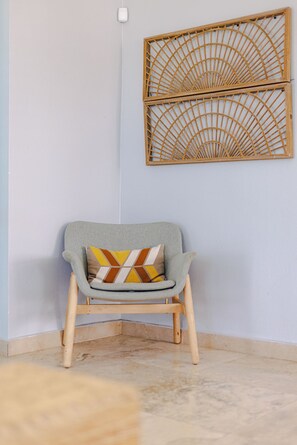 Una habitación de esquina con pared de color claro, una silla de madera con cojín y un panel decorativo en la pared.