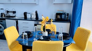 A modern kitchen with white cabinets, a black countertop, and a dining area with yellow chairs and a blue tablecloth.