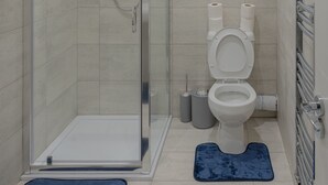 A modern bathroom with a glass-enclosed shower, a toilet, and a towel rack.