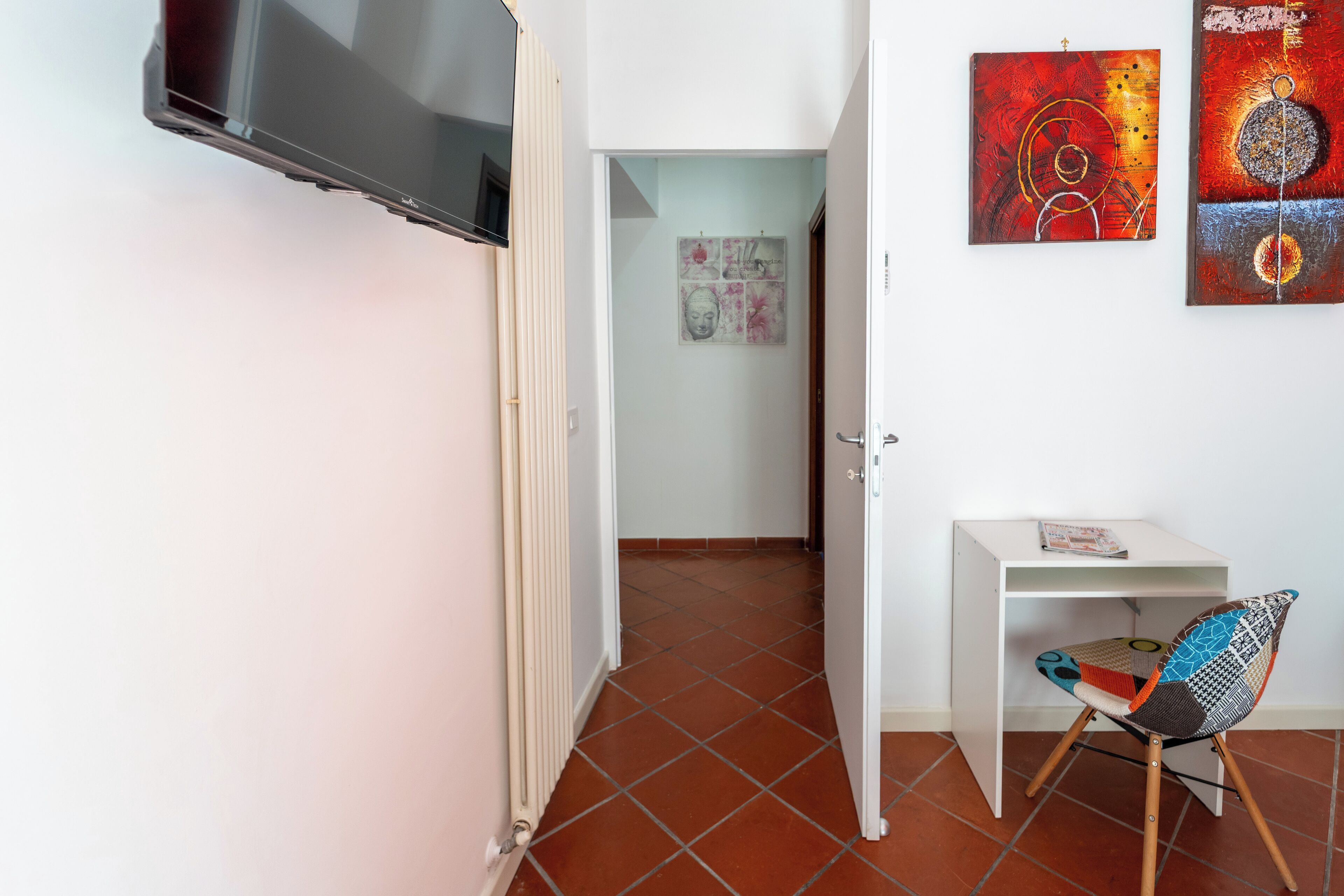 A room with a tiled floor, a white desk, a colorful chair, and a TV mounted on the wall.