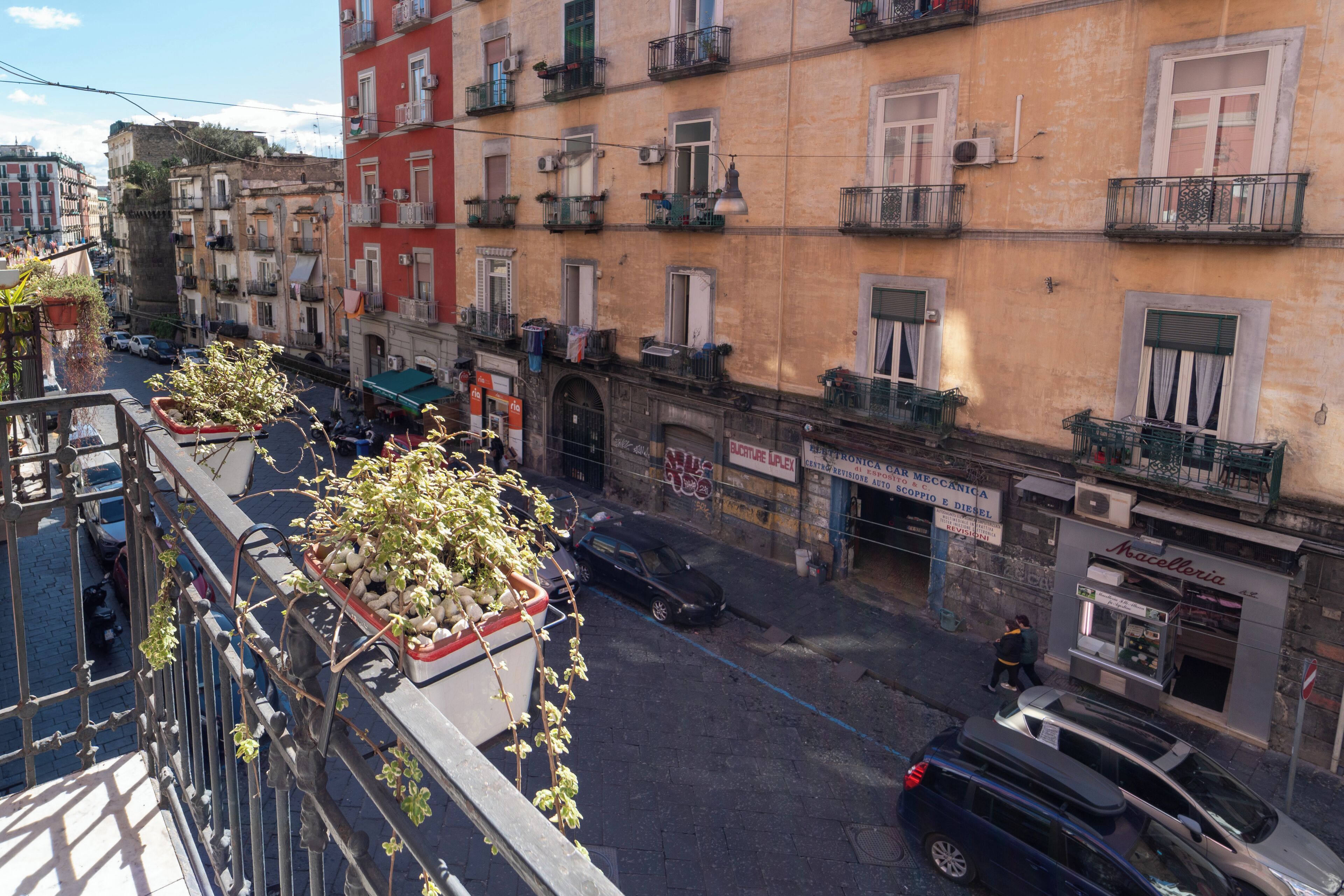 A narrow street lined with multi-story buildings, some with balconies and outdoor seating.