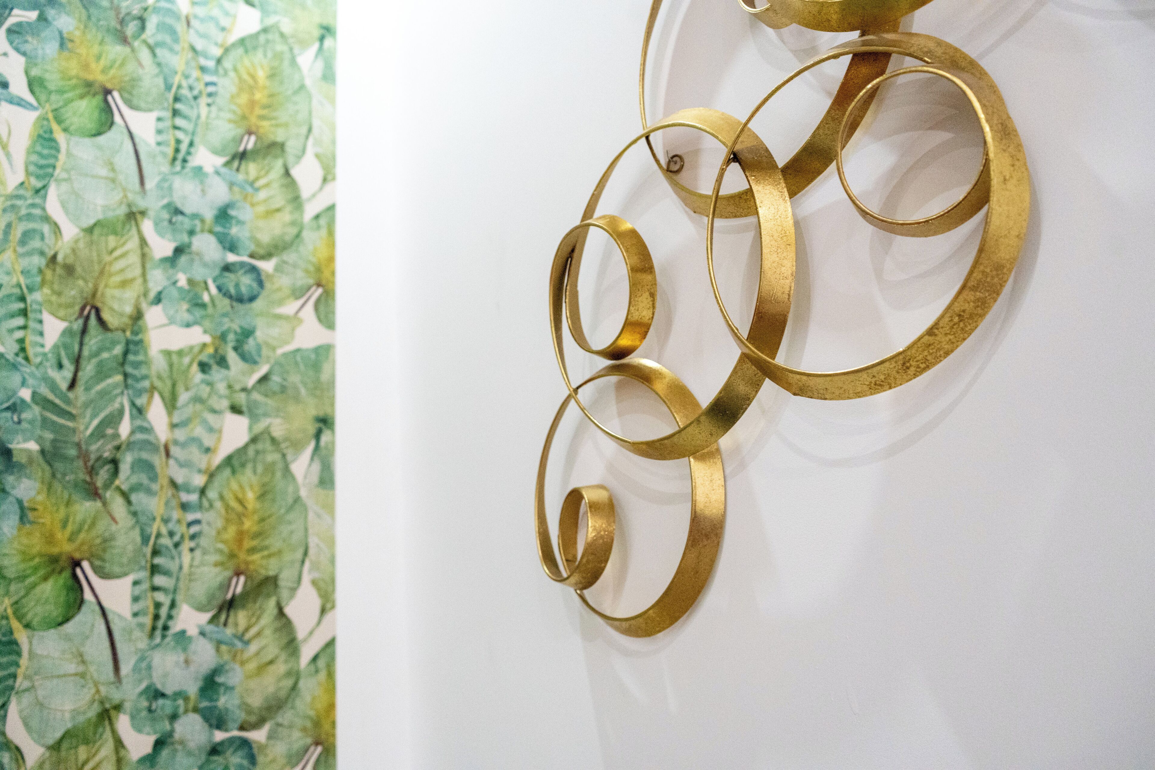 Una pared con estampado de papel tapiz floral y una escultura abstracta dorada.