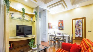 Un salon doté d’un téléviseur à écran plat, d’une table basse en verre, d’un canapé à rayures rouges, d’un coin repas avec une table et des chaises, et d’un tableau accroché au mur.
