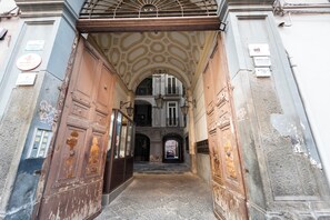 An arched entrance with rusted doors and a stone-paved path leading to a building with balconies and a central staircase. - Rosaroll 70 Apartment by Wonderful Italy (Naples)