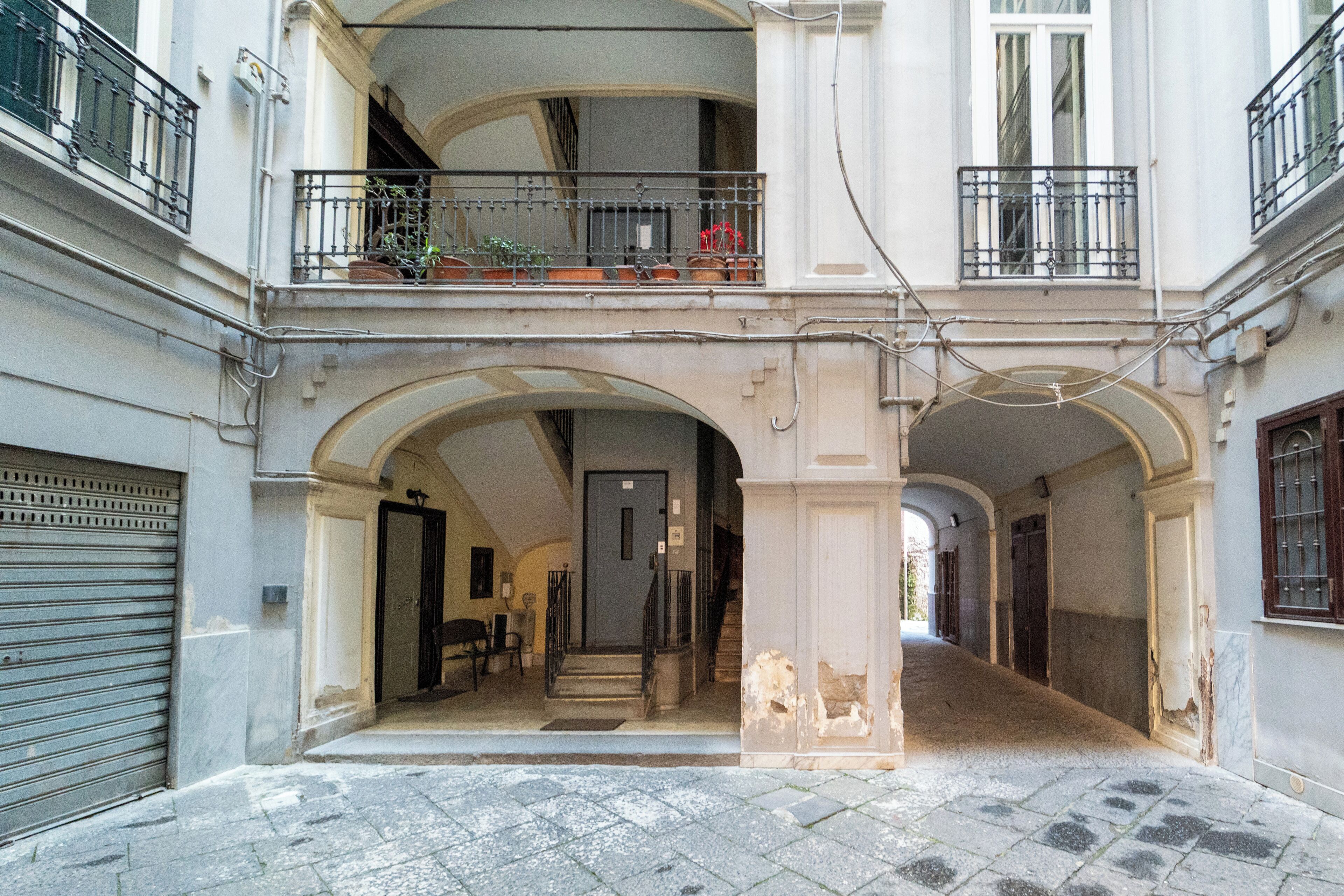 A building with a covered courtyard, a staircase leading to an upper floor, and a door at the end of the corridor.