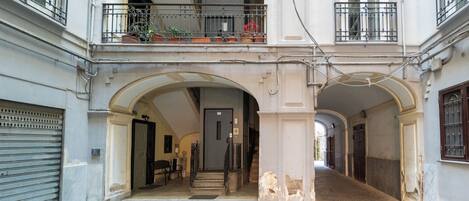 A building with a covered courtyard, a staircase leading to an upper floor, and a door at the end of the corridor.
