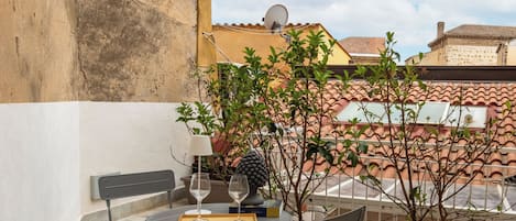 Ein kleiner Außenbereich mit Tisch und Stühlen, einem Blumentopf und Blick auf Gebäude im Hintergrund.