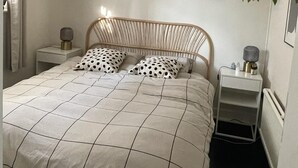 Ett sovrum med en säng, sängbord, en hängande lampa av rotting, inramade tavlor, en gitarr och hängande växter.