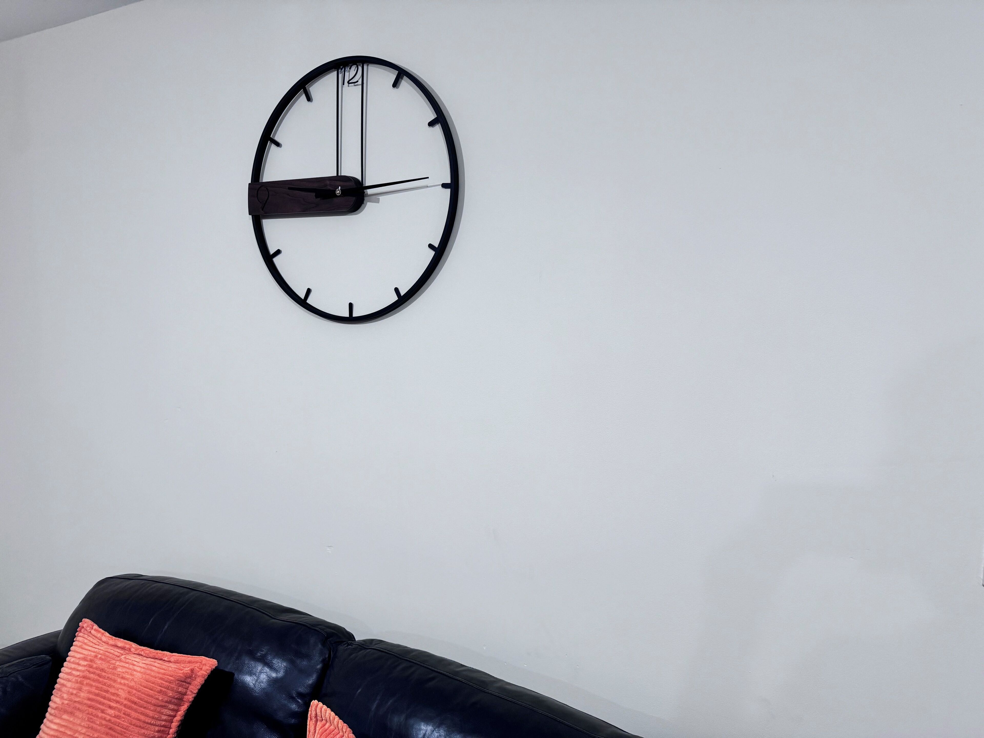 A modern wall clock with a minimalist design, mounted on a plain white wall.