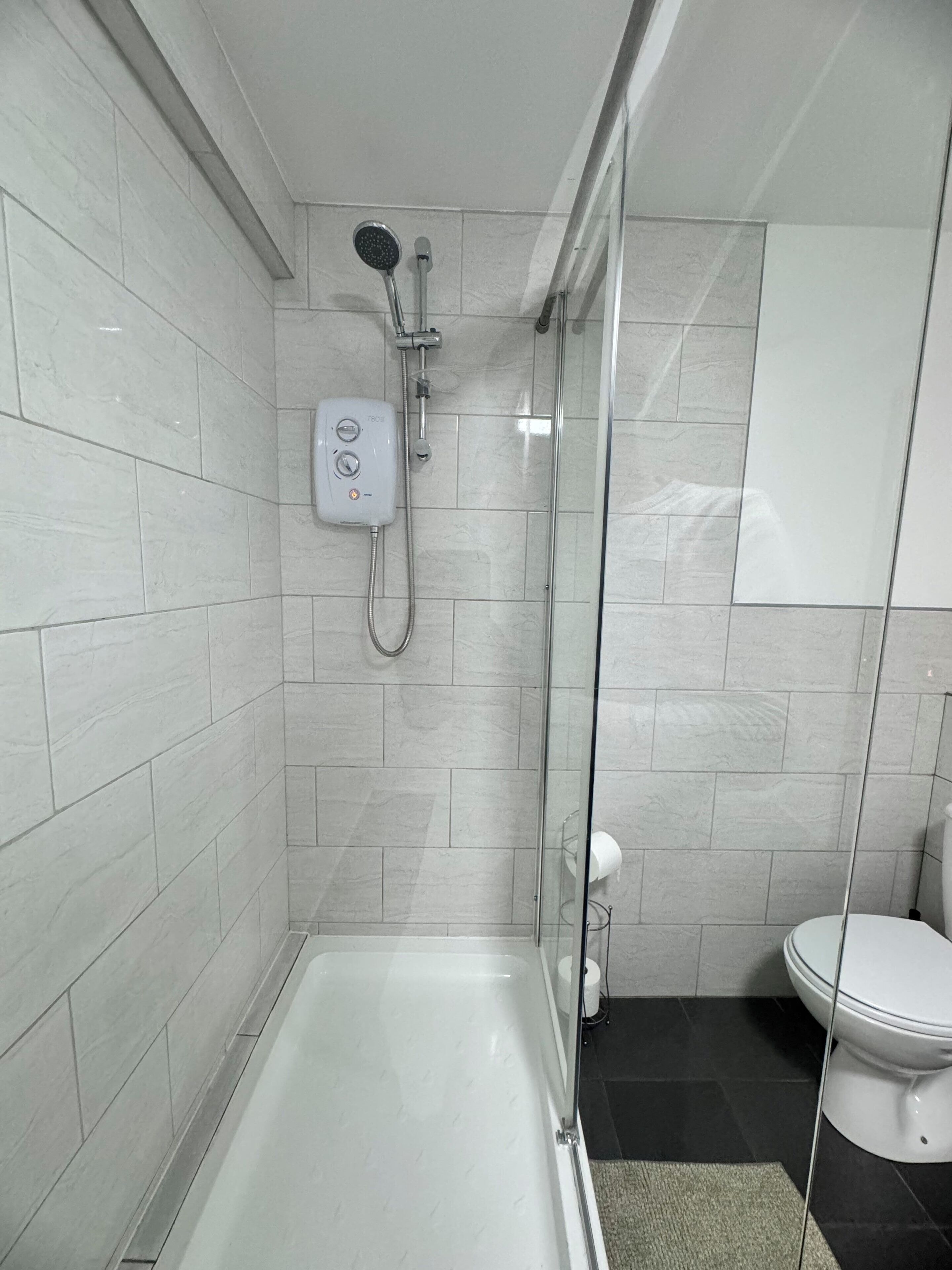 A modern bathroom with a glass-enclosed shower, a white toilet, and a tiled floor.
