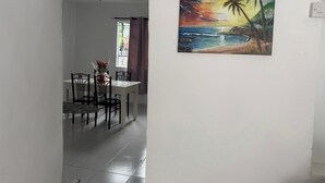 Un'area pranzo con tavolo e sedie, una finestra con tende e un quadro raffigurante un tramonto sull'oceano.