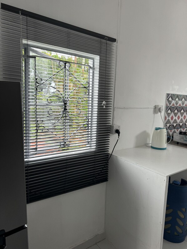 Un baño con ventana, hervidor y un cubo azul.