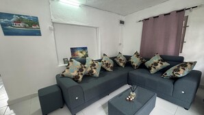 Un soggiorno moderno con un divano modulare grigio, numerosi cuscini decorati, un tavolino da caffè in vetro e due quadri appesi al muro.