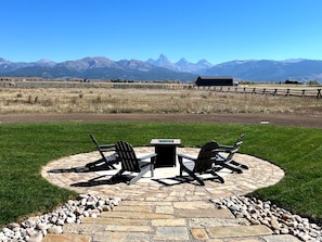 An outdoor patio with a stone table and chairs, surrounded by a stone border, with a mountain view in the background.