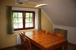 A dining area with a wooden table and chairs, a window with curtains, and a radiator. - Kalkwerk Vacation Rental (Thum)