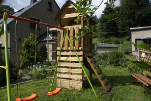 A wooden play structure with a slide and swings in a backyard. - Kalkwerk Vacation Rental (Thum)