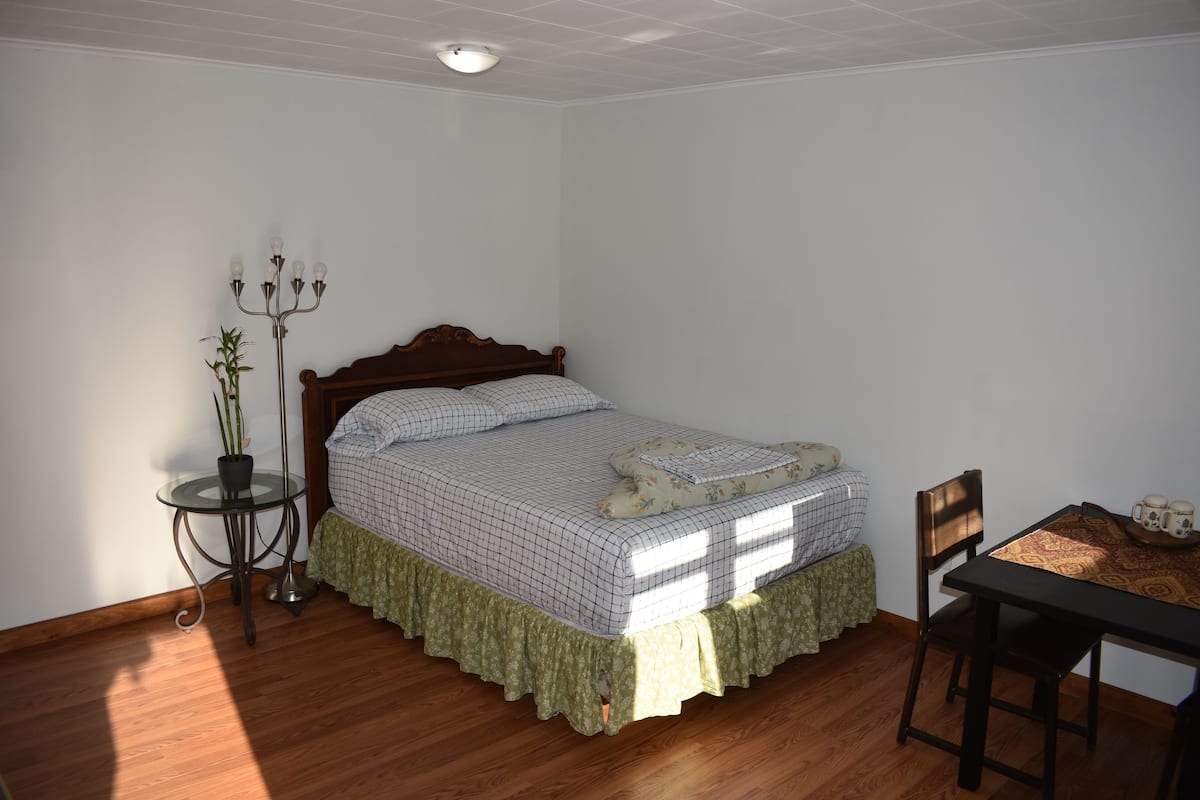 Un dormitorio con una cama de madera, una mesita de noche con una lámpara y una silla.