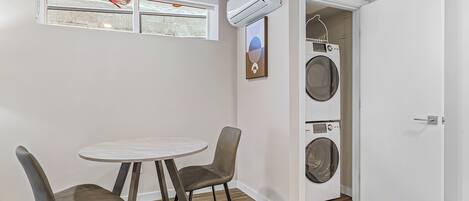 A compact living space with a dining area, a washing machine, and a door leading to another room.