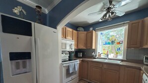 Una cocina con armarios de madera, un refrigerador, un microondas, un horno y una ventana con vista a un jardín.