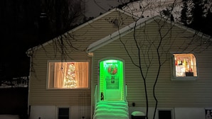 Una casa con puerta iluminada en verde, un árbol de Navidad a la vista y una puerta de garaje.