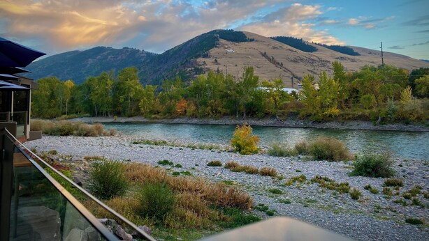 Un río con orilla rocosa, rodeado de árboles y una montaña al fondo.