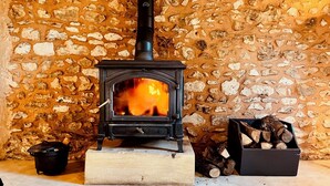A stone wall interior with a wood-burning stove. - Vue Épique : Gîte Magnifique (Capdrot)