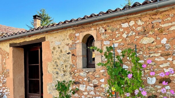 A rustic stone building with a tiled roof, a wooden door, and a window. - Vue Épique : Gîte Magnifique (Capdrot)