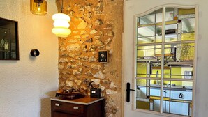 A stone wall, a wooden cabinet, a door with glass panels, and a hanging light fixture. - Vue Épique : Gîte Magnifique (Capdrot)