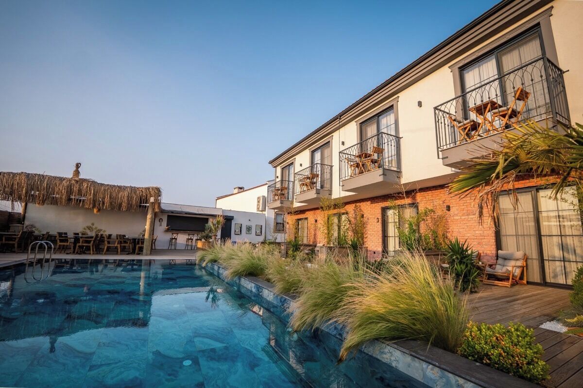 Una piscina con cubierta de madera, una estructura de techo de paja y un edificio con balcones y ventanas.