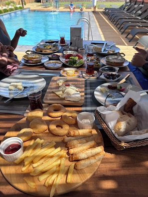 A poolside dining area with a variety of dishes, including fried items and salads, and a view of the pool in the background. -  Nüans Küçükköy (Ayvalik)