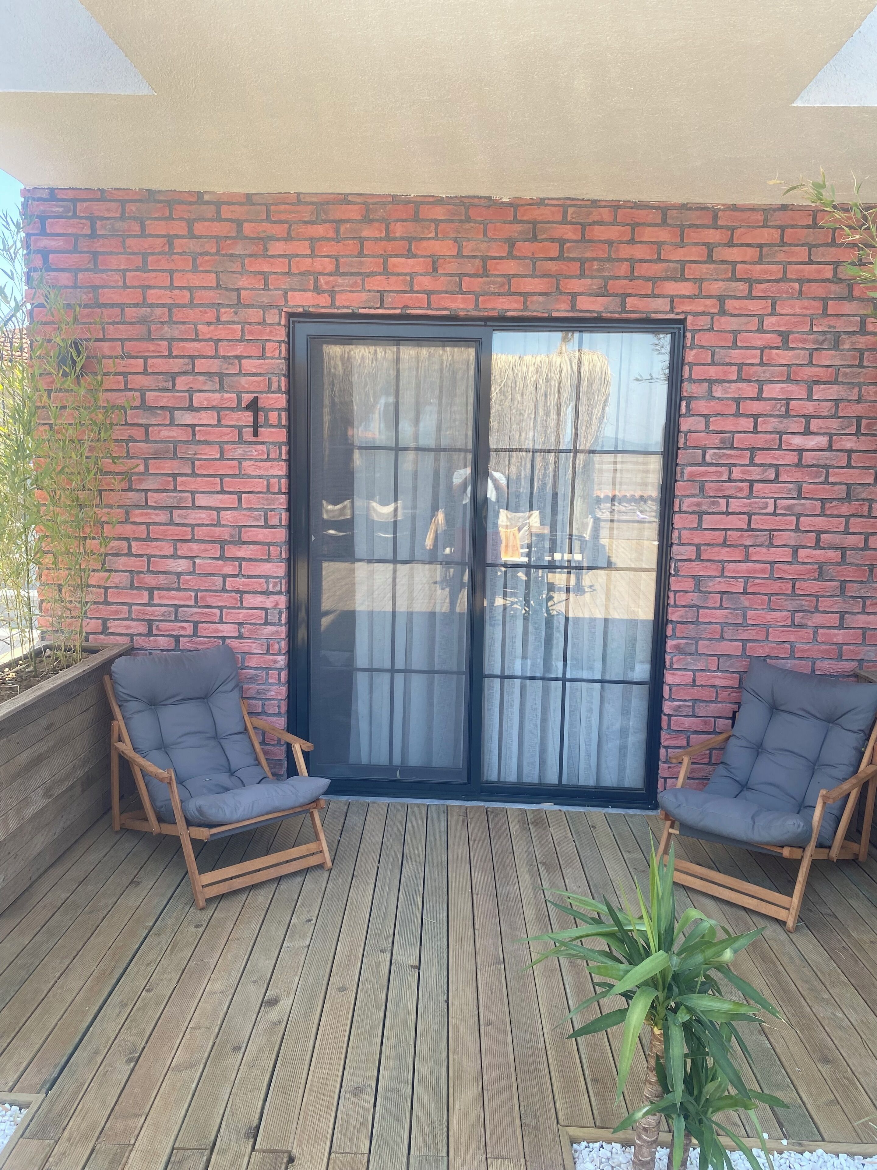 A wooden deck with two wooden chairs, a brick wall, and a sliding glass door.