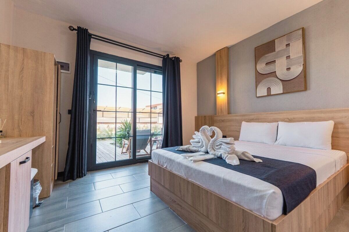 Habitación de hotel con cama, un escritorio de madera, una puerta corrediza de vidrio a un balcón y una obra de arte abstracto colgada en la pared.