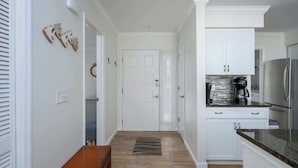 A hallway leading to a kitchen with white cabinets, a coffee maker, and a refrigerator. - Luxury 2BR Shipyard Villa: Golf Views, Heated Spa & Walk to Beach (Hilton Head Island)