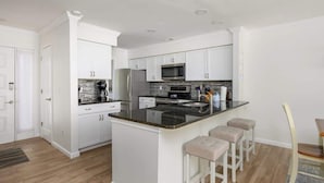 A modern kitchen with white cabinetry, a central island with bar stools, and a stainless steel refrigerator. - Luxury 2BR Shipyard Villa: Golf Views, Heated Spa & Walk to Beach (Hilton Head Island)