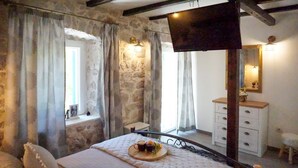 Una camera da letto con parete in pietra, un letto con vassoio di bevande, un comò e uno specchio.