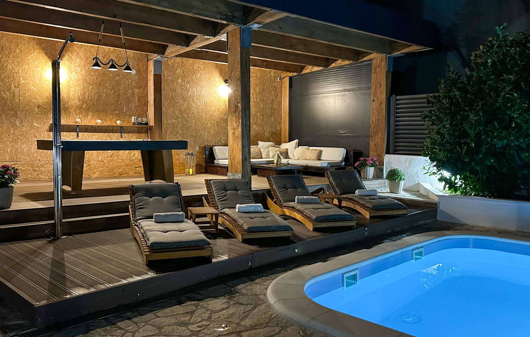 An outdoor pool area with lounge chairs, a wooden deck, and a seating area with cushions.