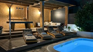 Area piscina esterna con lettini, un solarium in legno e una zona relax con cuscini.