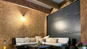 Un soggiorno accogliente con soffitto in legno, un'ampia porta scorrevole nera, un divano bianco con cuscini, un tavolino da caffè in legno e una piccola pianta in vaso.