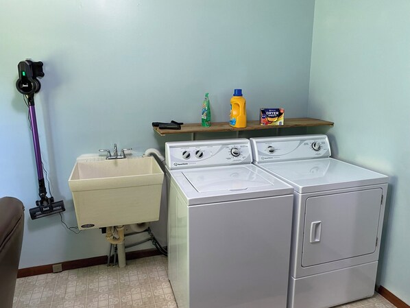 A laundry area with a washing machine, a sink, and a vacuum cleaner.
