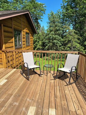 A wooden deck with two rocking chairs and a small table, overlooking a forested area.