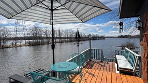 A wooden deck with a table and chairs, a large umbrella, and a view of a body of water. - Bay Loft Couples Retreat – Nature, Comfort & Charm (Stevens Point)