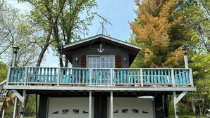 A two-story house with a balcony, garage, and stone foundation. - Bay Loft Couples Retreat – Nature, Comfort & Charm (Stevens Point)