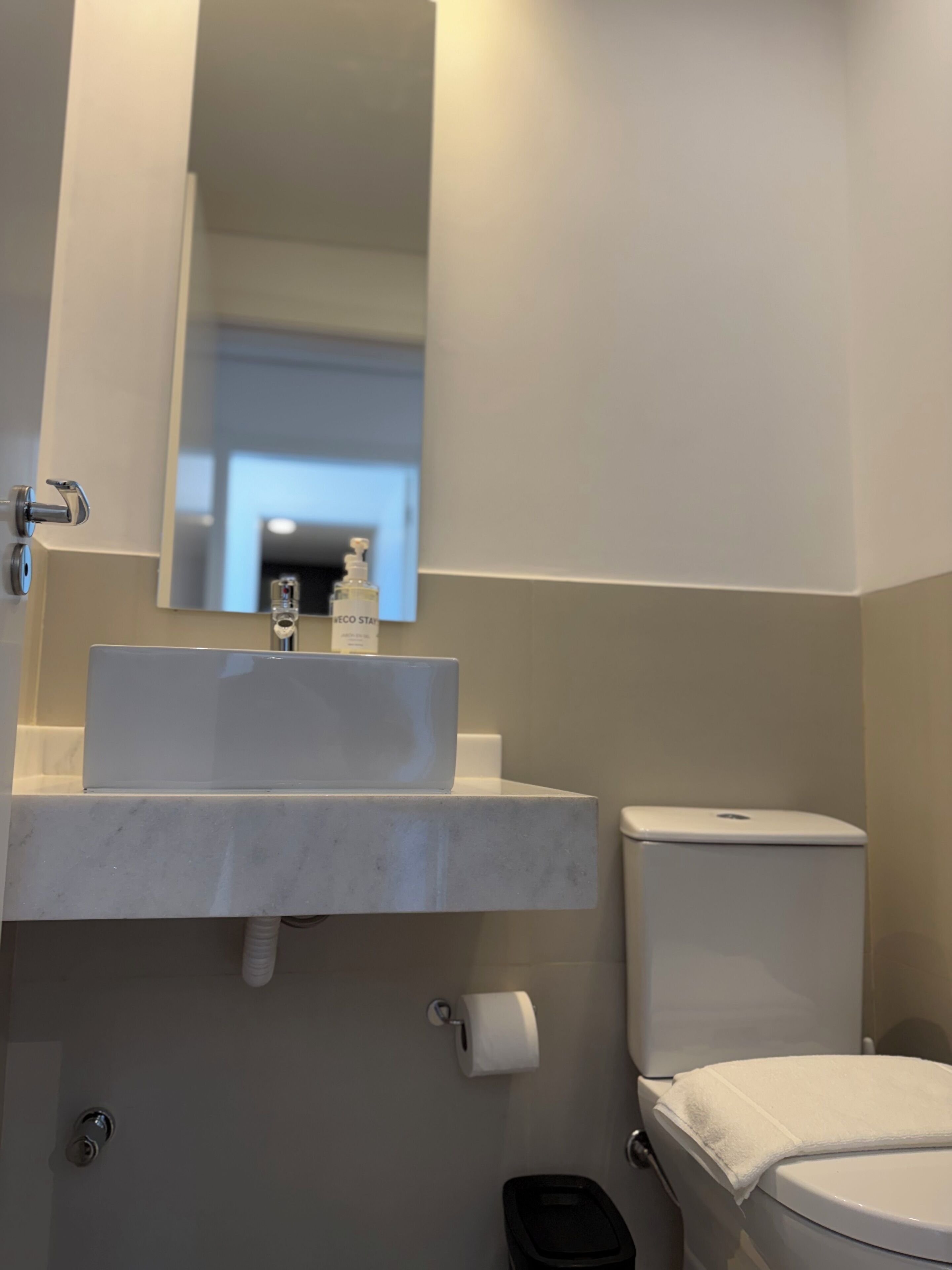 A bathroom with a white sink, mirror, toilet, and a trash bin.