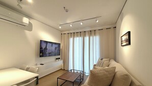 A modern living room with a flat-screen TV, a sofa, a coffee table, and a dining area.