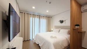 A hotel room with a bed, a TV mounted on the wall, a ceiling fan, and a window with curtains.